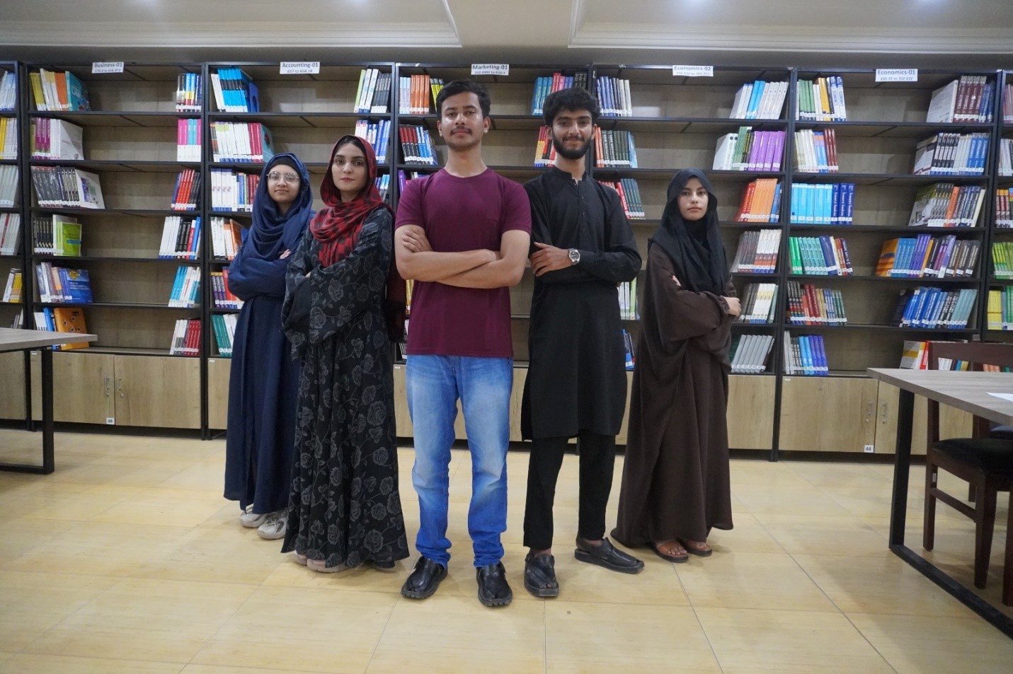 Group of UOR students standing together in a library surrounded by bookshelves.
